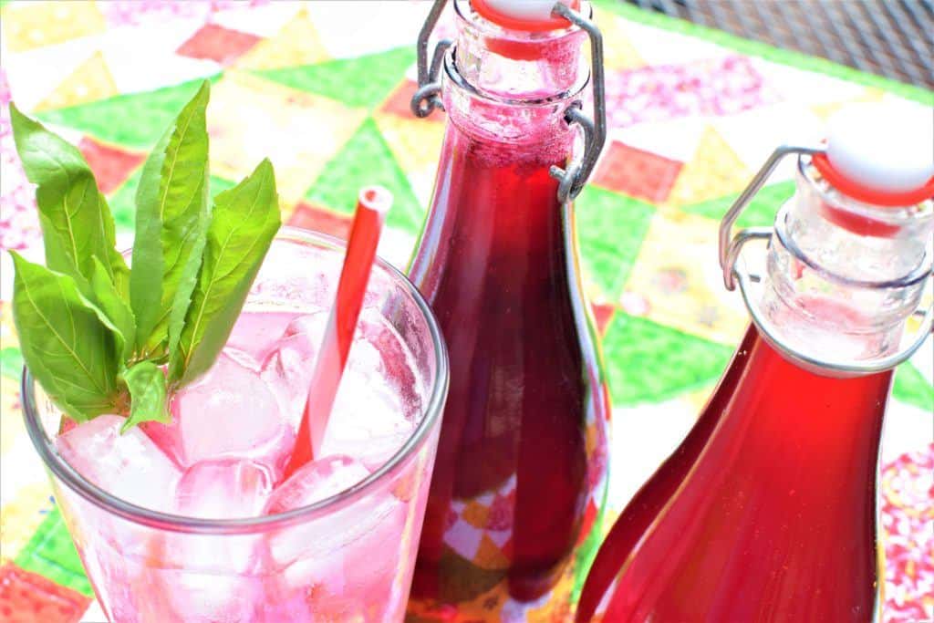 Two bottles of shrubs with a glass filled with ice and a pink drink.