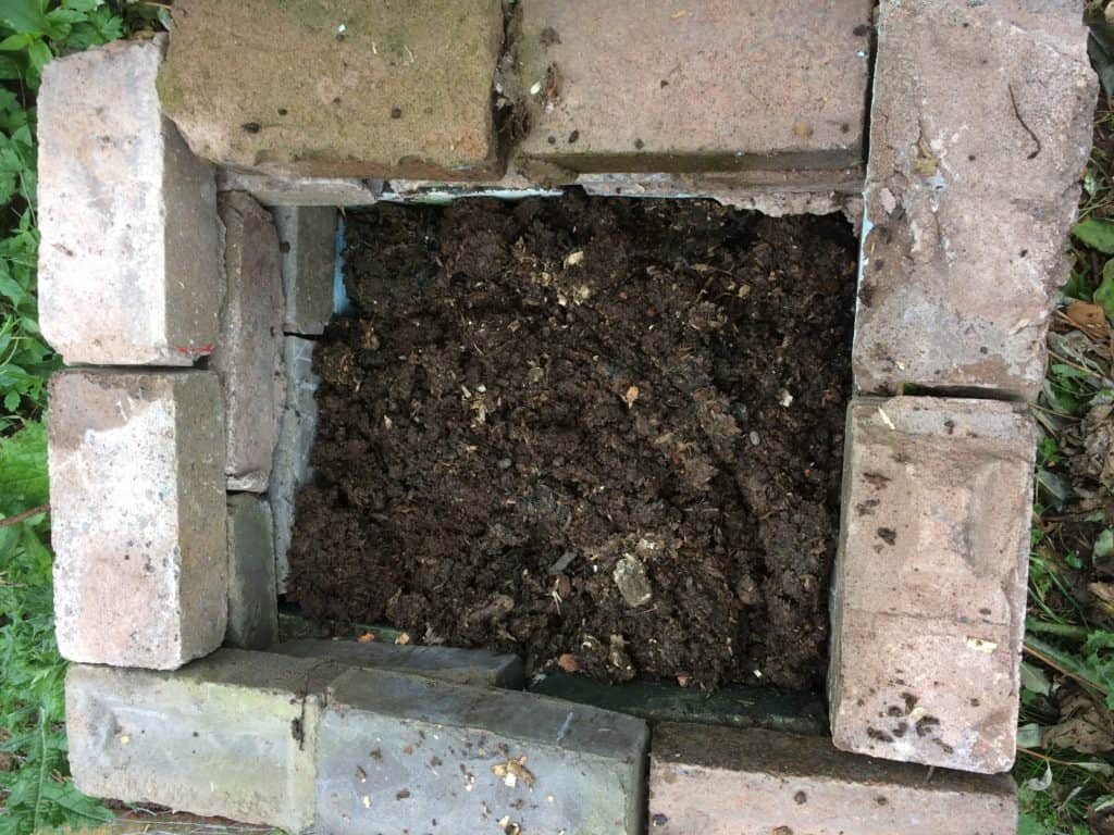 A heap of compost has been added to a newly constructed hotbed.