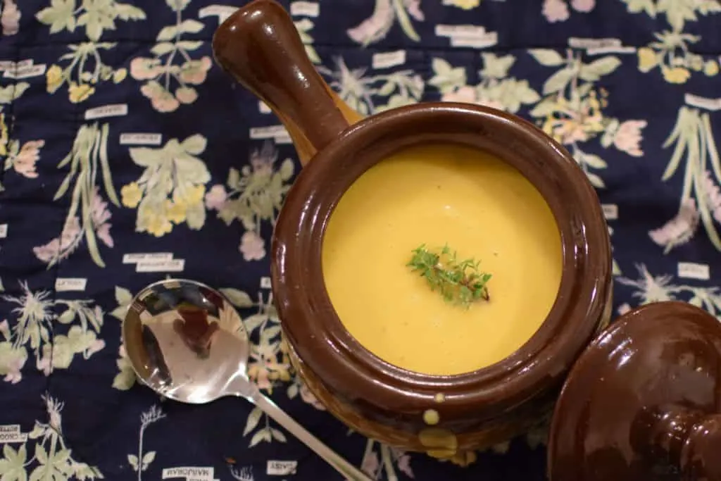 A crock of pumpkin soup on top of a placemat.
