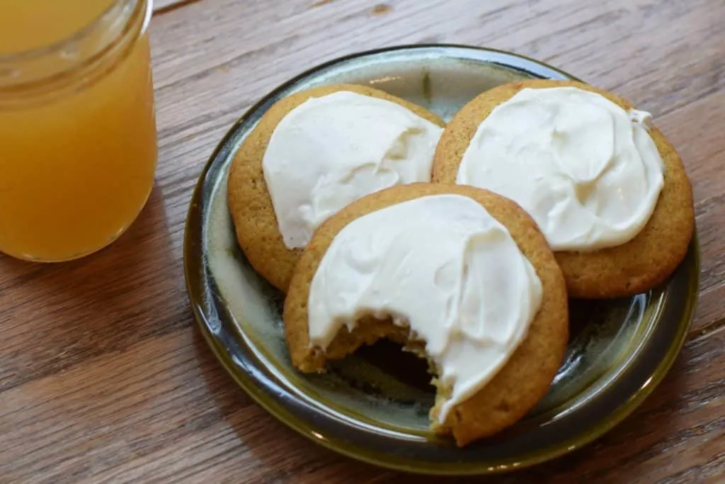 Three pumpkin cookies on a plate with a bite taken from one.