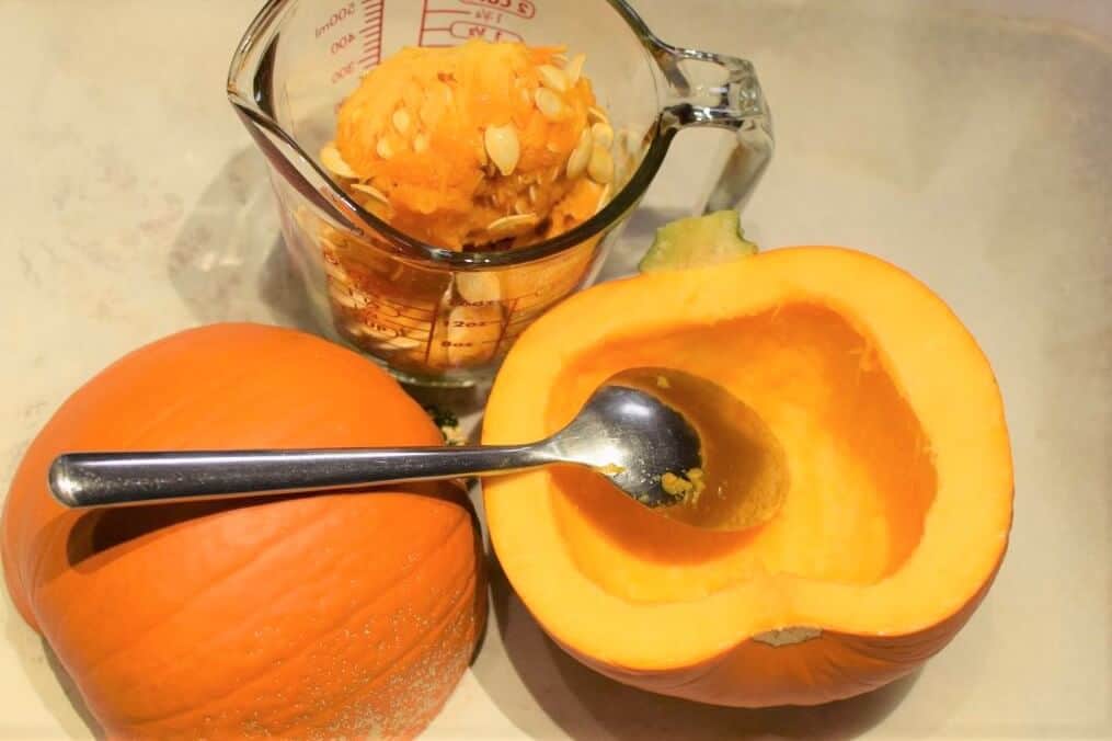 A small pumpkin cut in half and scooped out, seeds saved in a glass measuring cup.