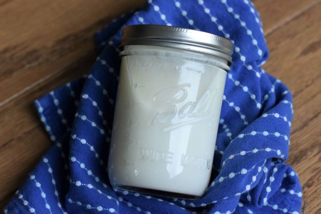 A jar of homemade cultured buttermilk on top of a blue kitchen towel.