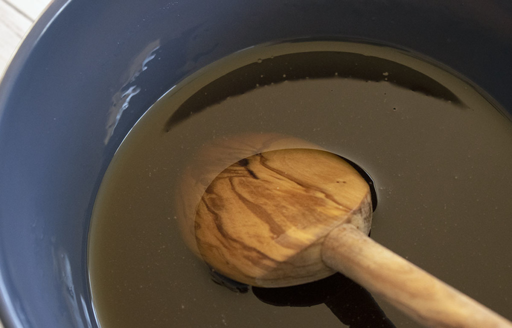 A blue bowl with hot maple syrup which will be made into maple cream. There is a wooden spoon in the syrup.