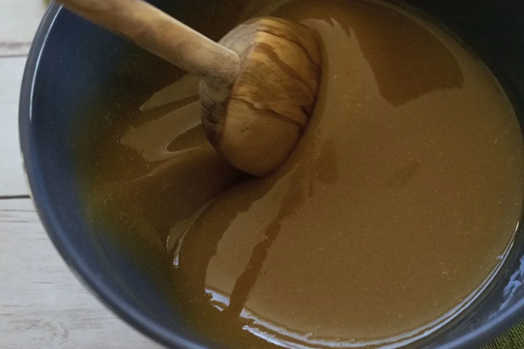 A bowl of maple syrup being stirred by a wooden spoon.