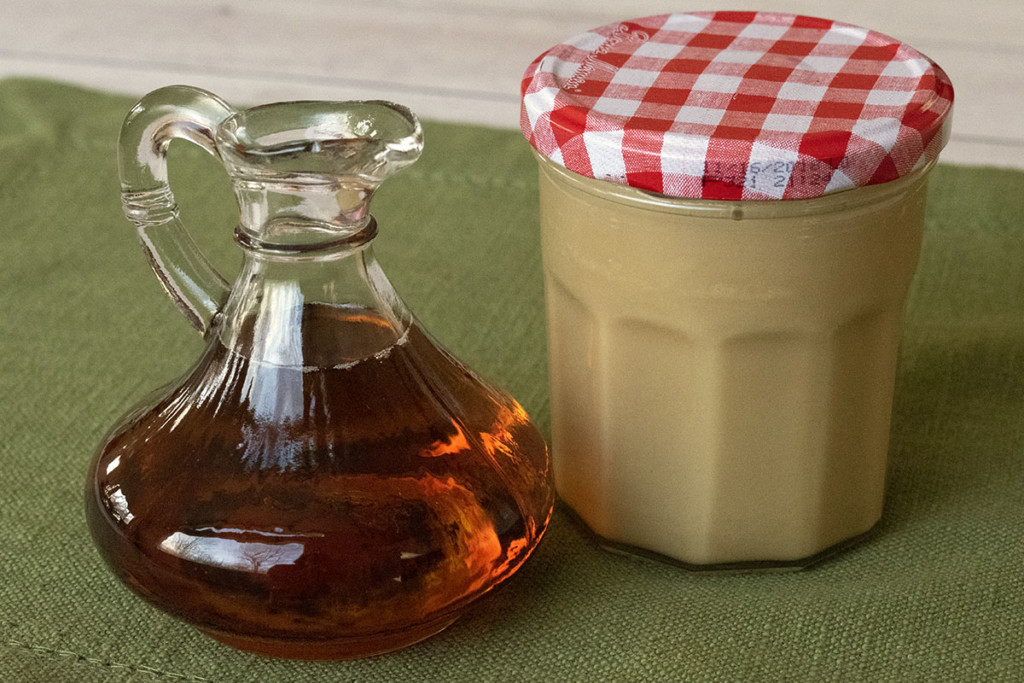 A jar of maple cream next to a small decanter of maple syrup.