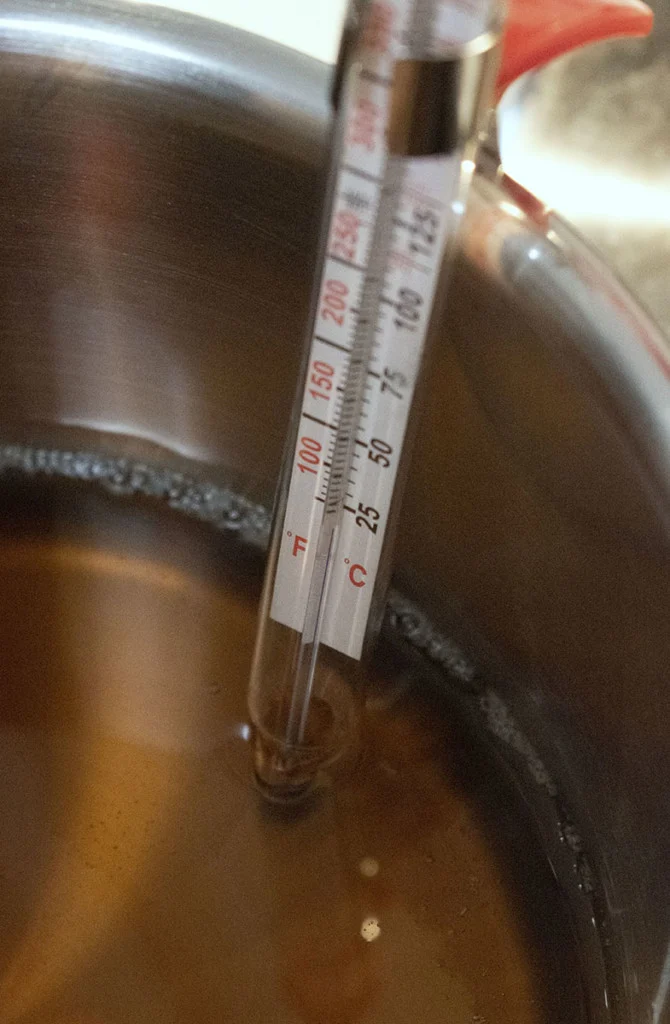 A candy thermometer in a pan of maple syrup.