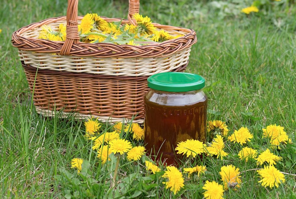 Jar of honey next to a basket of dandelion blooms. 