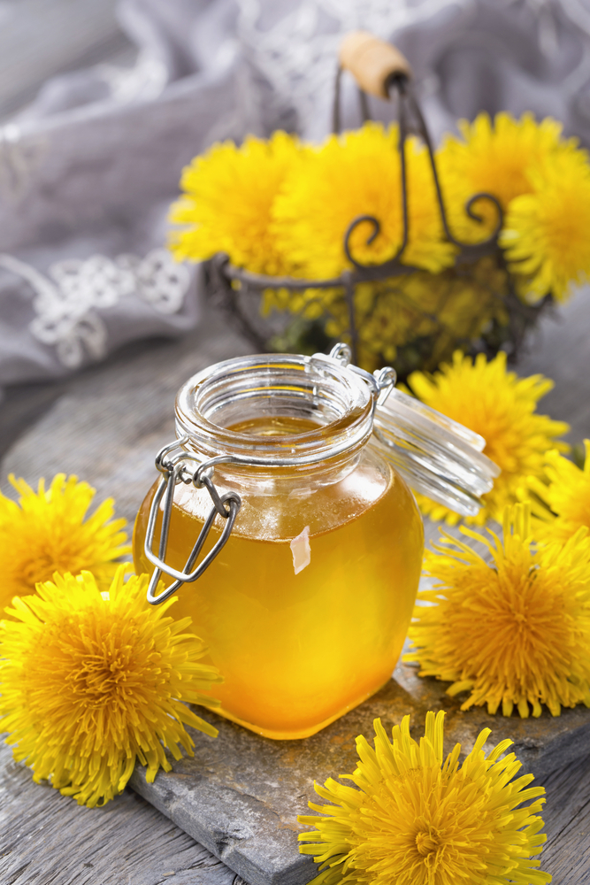 Jar of dandelion jelly with blossoms next to it 