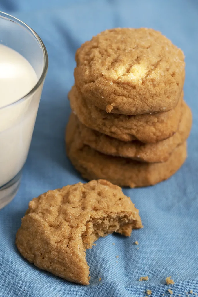 Stacked peanut butter cookies next to a glass of milk. 