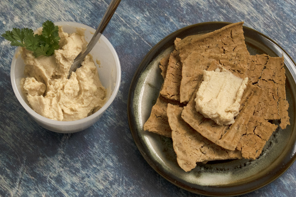 Sourdough discard crackers on a plate with a cup of hummus next to the plate.
