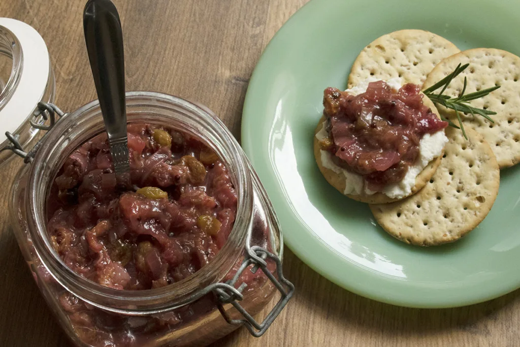 Rhubarb chutney in a jar with crackers on a plate next to it.