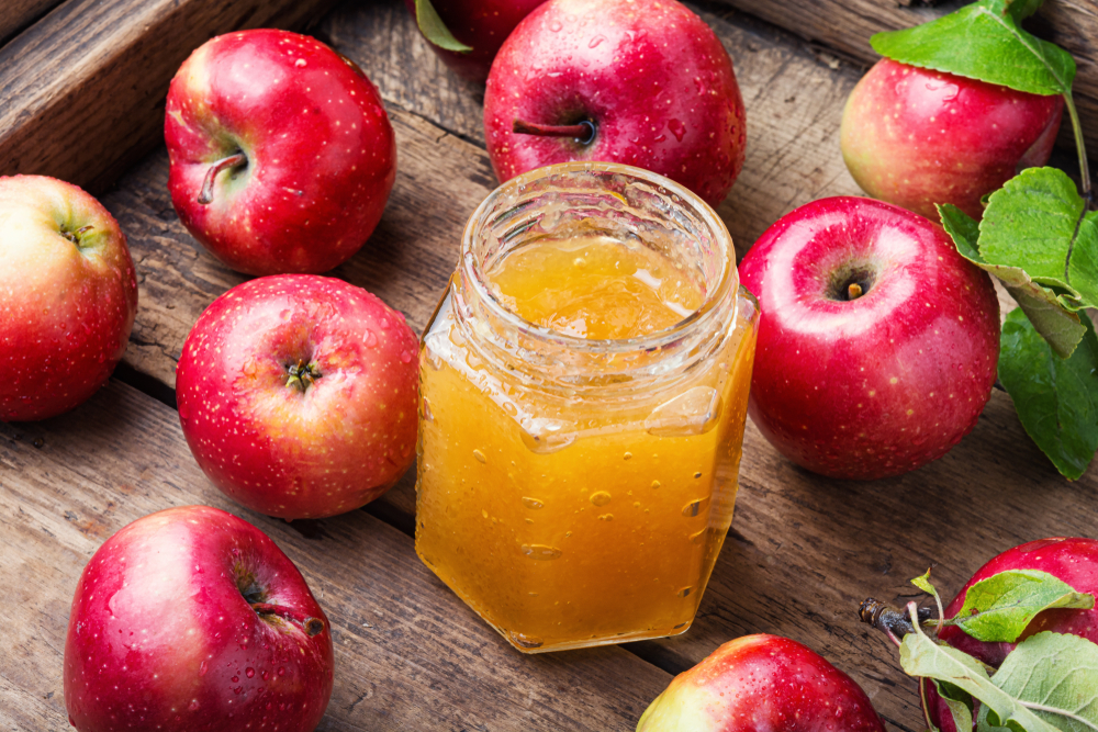 A jar of apple jelly surrounded by fresh apples.