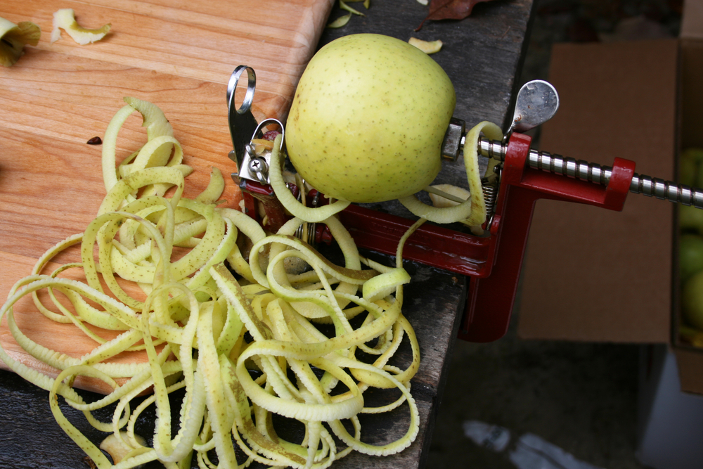An apple peeler in use with lots of peeled apple skins, a peeler is used when preserving apples.