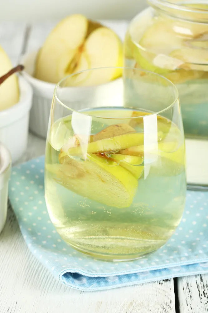 A glass of homemade apple wine with apple slices in it.