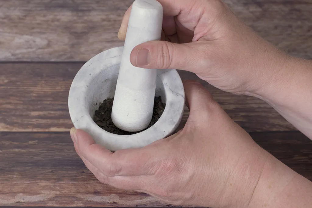 Hands hold a mortar and pestle which is filled with banana peel fertilizer powder.