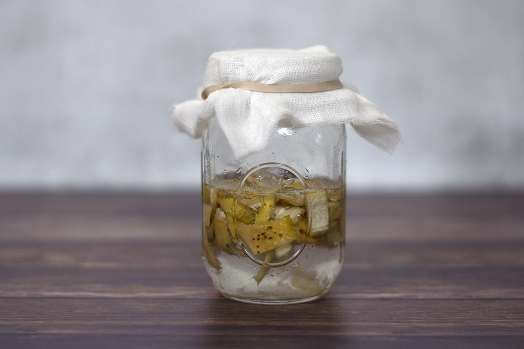 A jar filled with water and chopped banana peel with cheesecloth over the top of it.