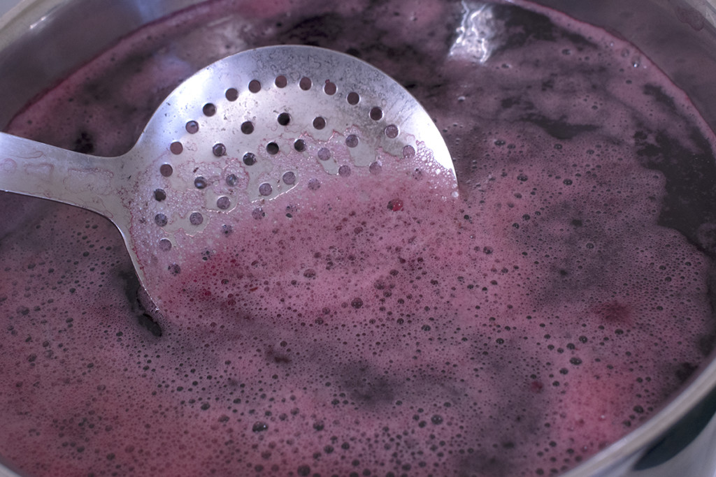 A skimmer spoon is used to remove the foam from the surface of the beet water.
