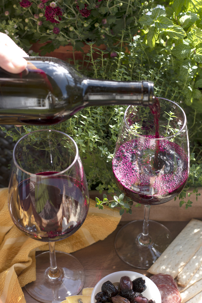 A hand pours two glasses of finished beet wine.