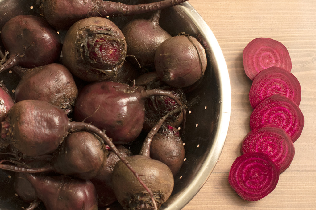 A colander with washed beets and a sliced beet on the counter.