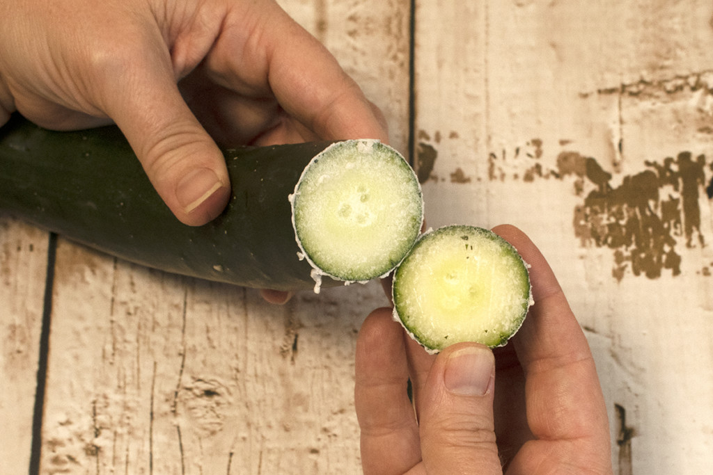 Hands holding cucumber with sliced tip. 