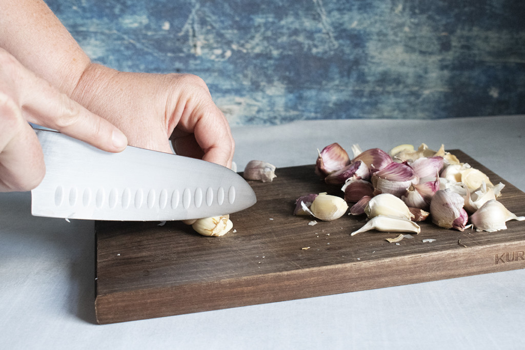 Hands using a knife to remove brown spots from a clove of garlic,