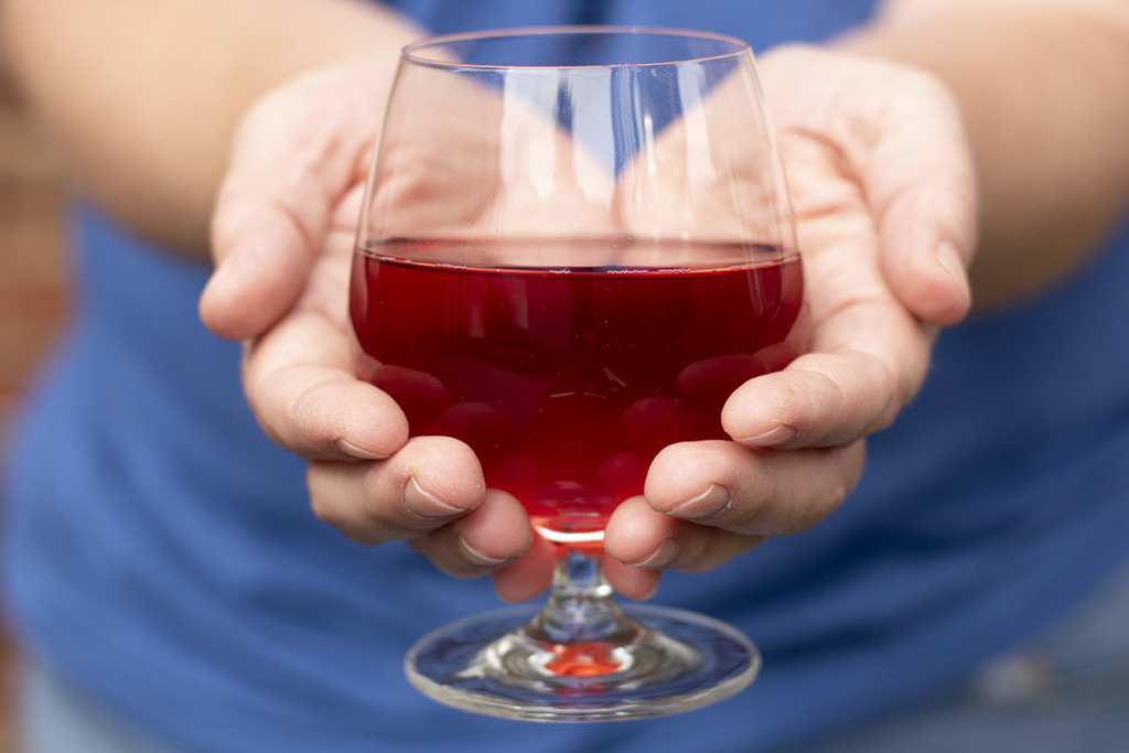 Two hands cupping a glass of blueberry mead