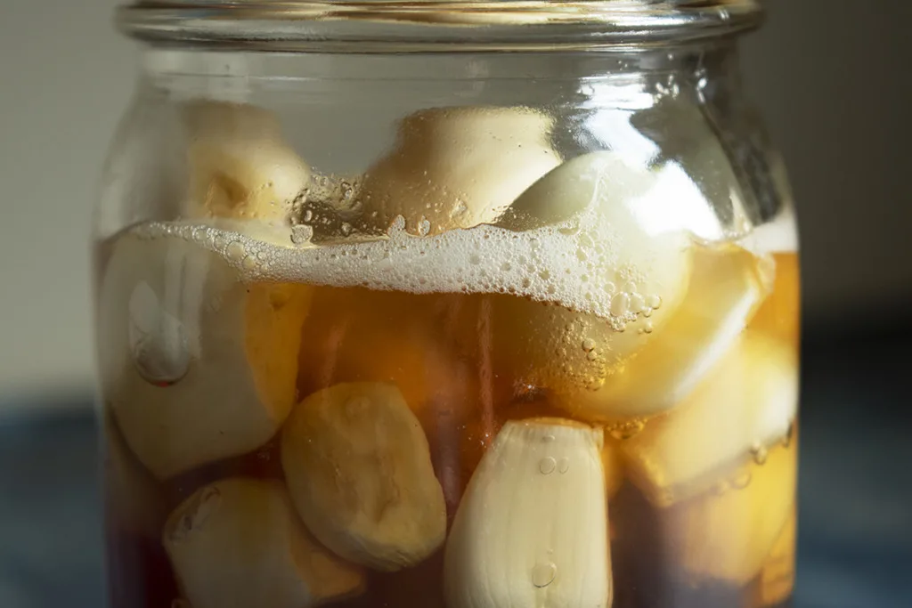 Jar of honey and garlic with many tiny bubbles on the surface.