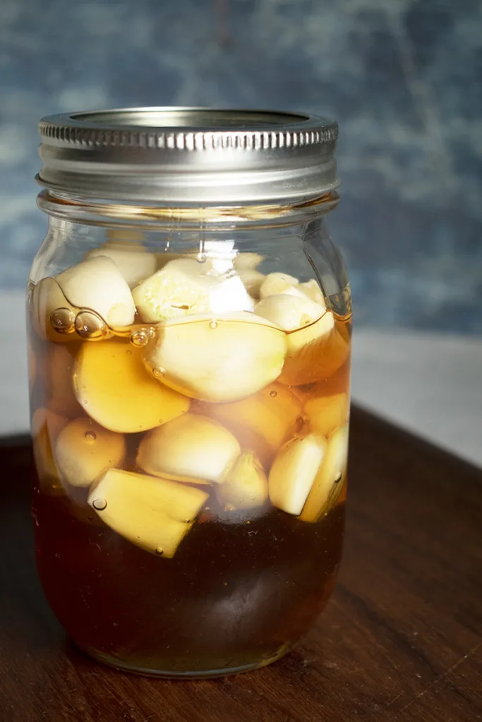 A jar of honey with garlic cloves floating in it. 