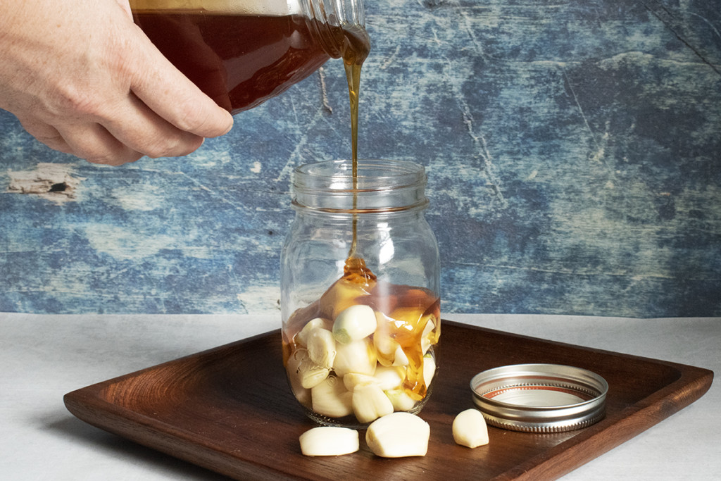 Pouring honey into a jar of peeled garlic cloves.