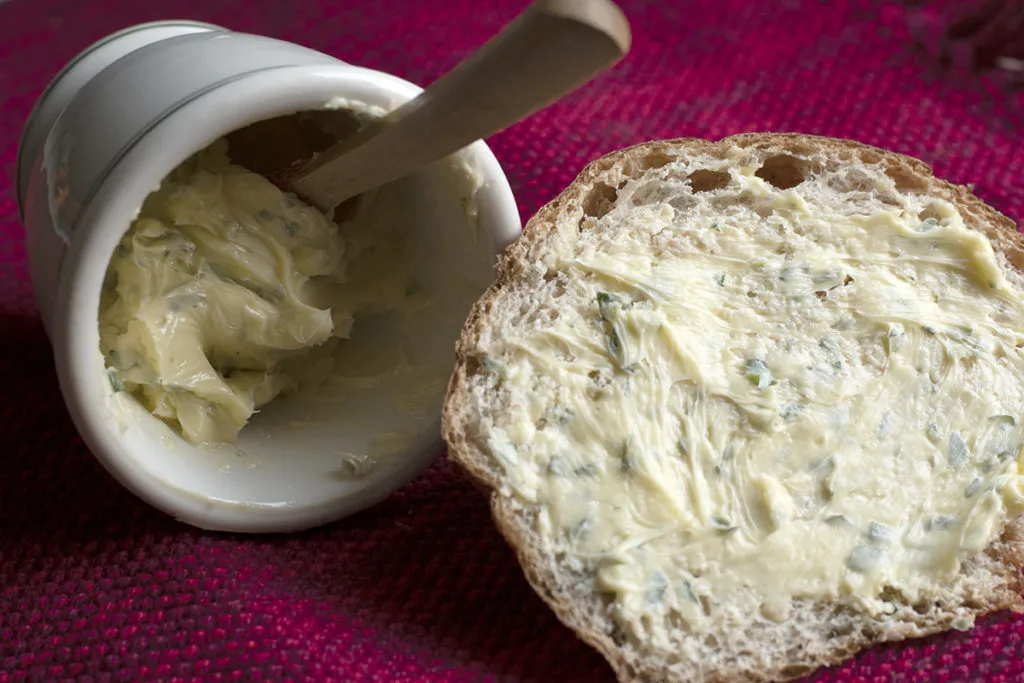 A small dish of compound butter and a slice of bread spread with the butter.