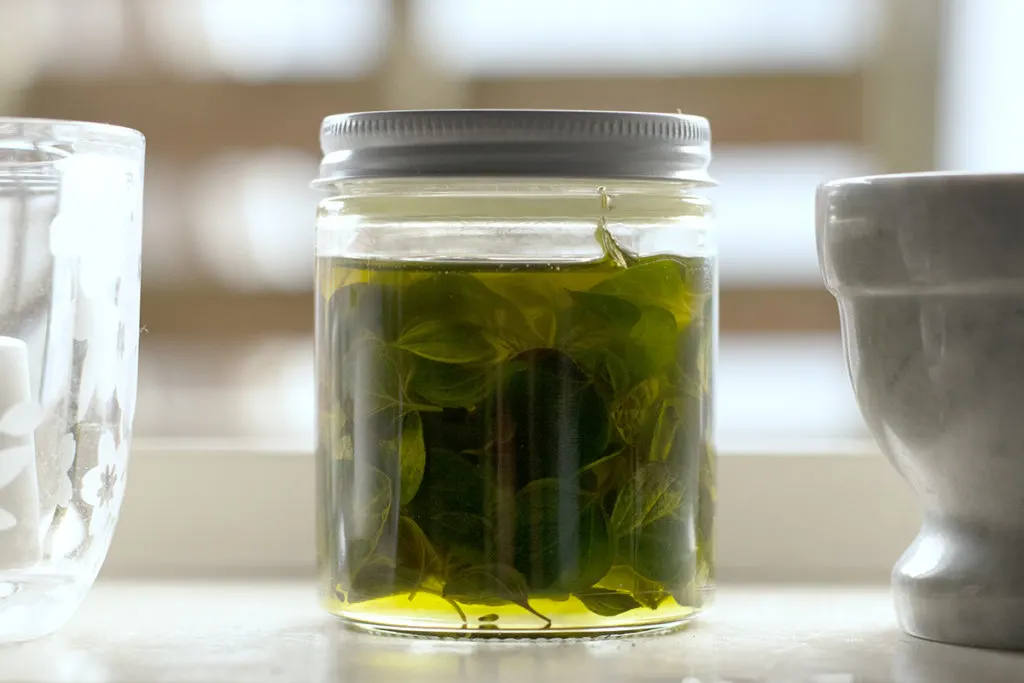 A small clear jar is filled with olive oil and oregano leaves.
