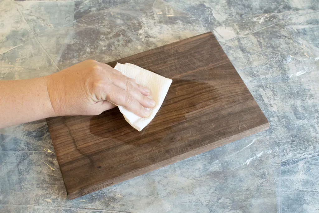  A hand is pictured applying cutting board oil to a wooden cutting board.