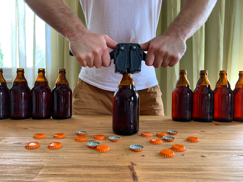 A man uses a bottle capper to put a cap on a bottle of homebrewered beer.