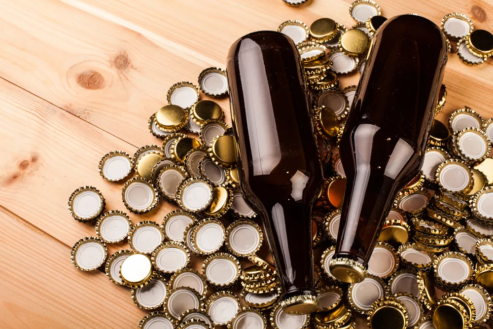Two beer bottles lie on top of a bed of bottle caps.