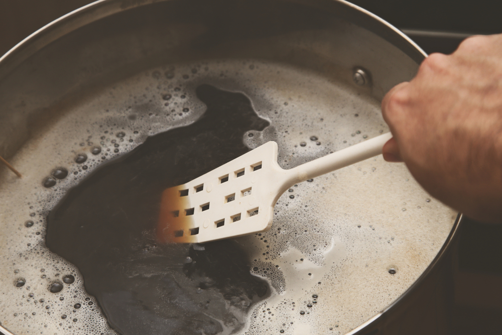 A hand uses a paddle to stir wort.
