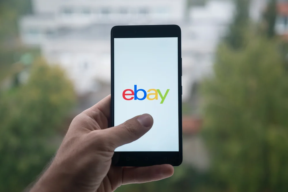 A hand holding up a smart phone with the ebay logo on the screen.