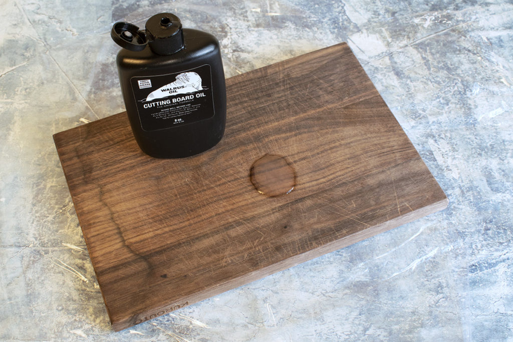 A wooden cutting board with a bottle of Walrus Oil cutting board oil on it and a bit of the product applied.