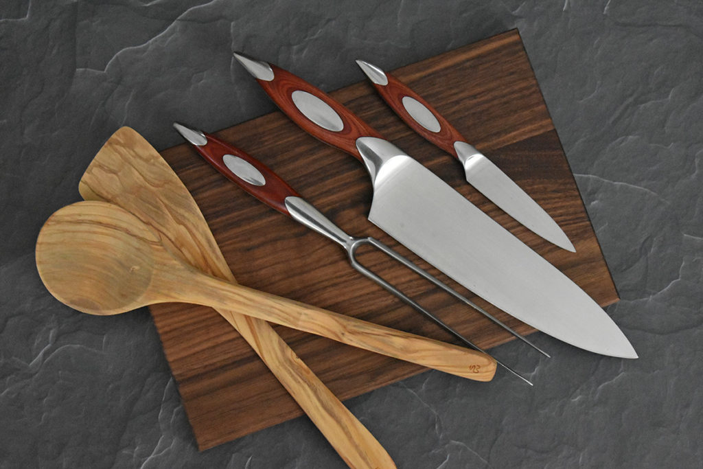 Knives and wood spoons on a cutting board.