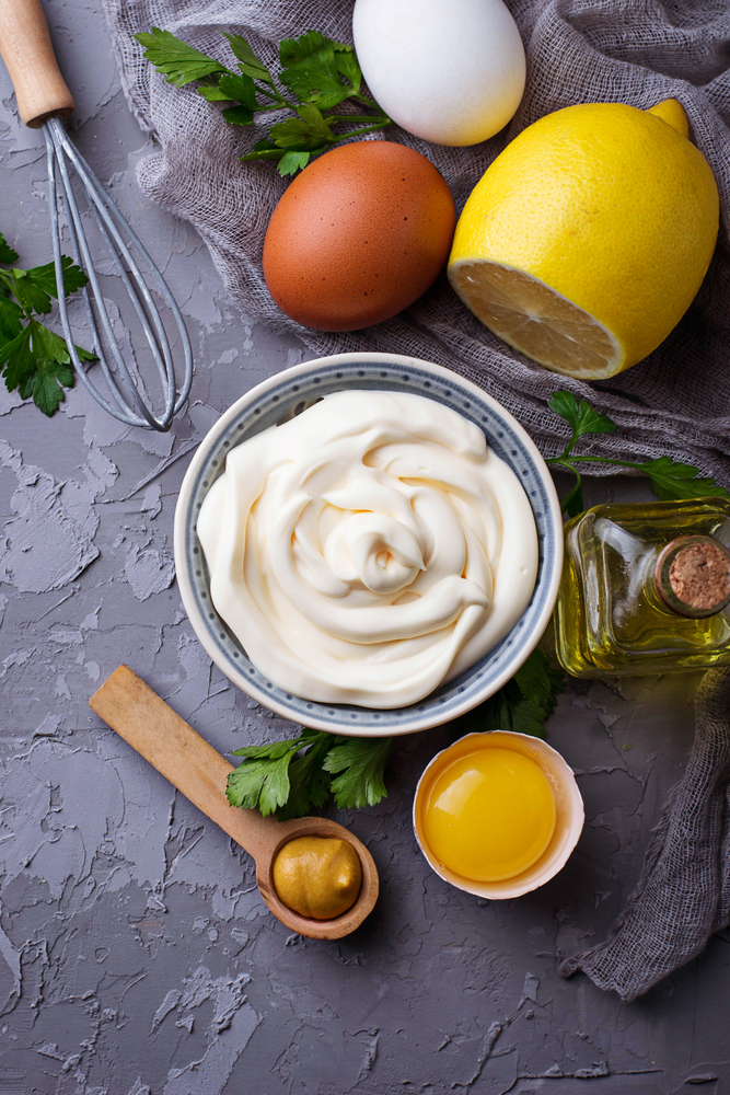 Homemade mayonnaise in a dish with ingredients used nearby. 