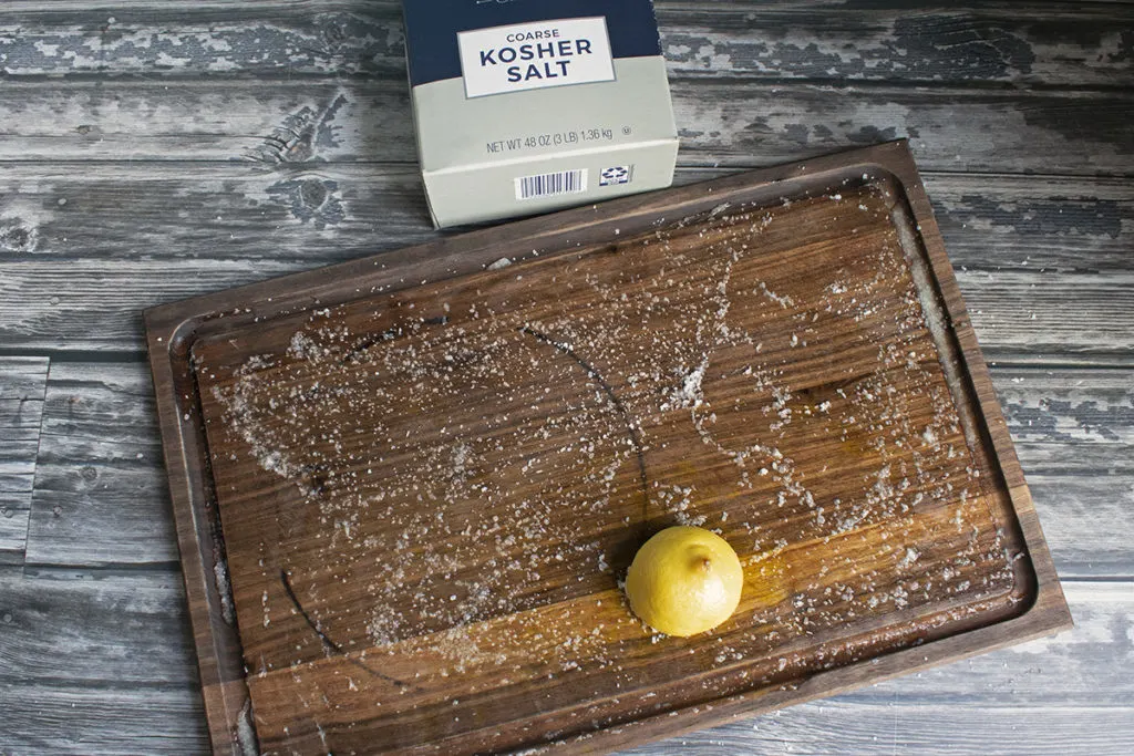 Wooden cutting board sprinkled with coarse kosher salt with a lemon half resting on top.
