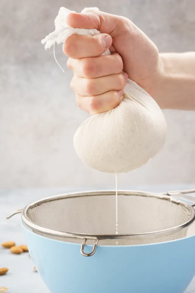 A hand is squeezing a bag of almond mash to make almond milk.