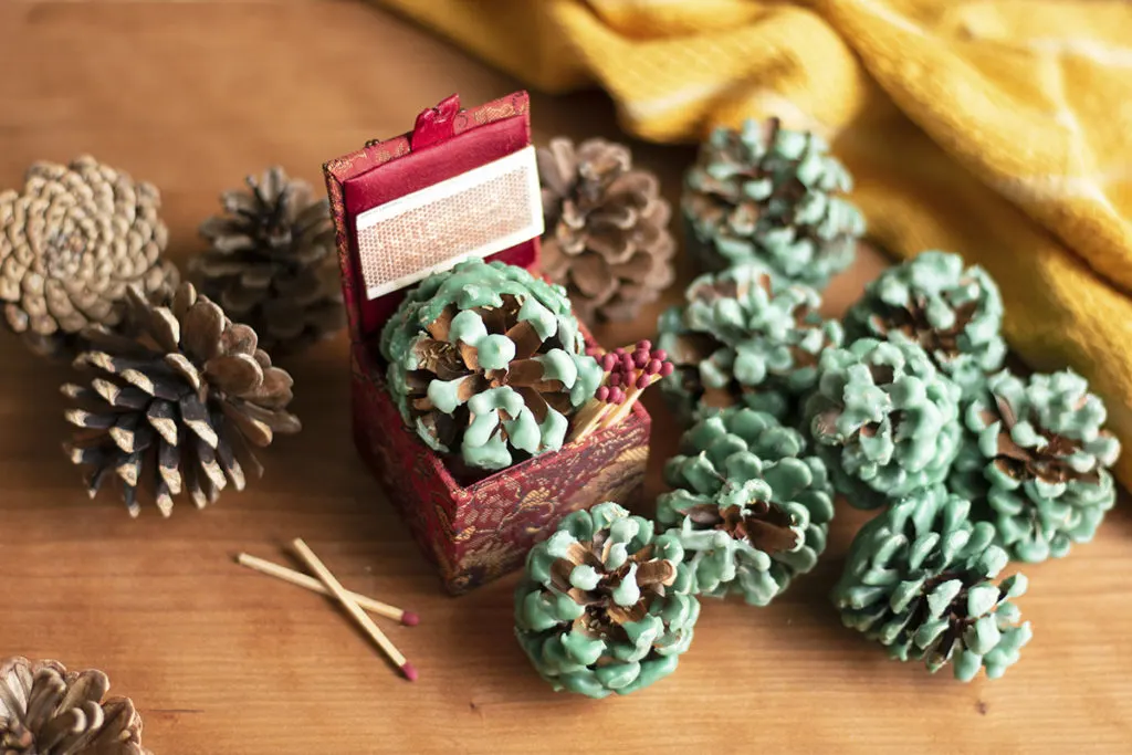 Several wax-covered pine cones are scattered on a table next to a decorative box of matches.