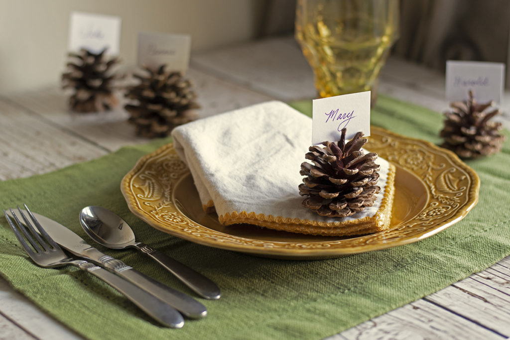 A place setting is showing with a pine cone used as a place setting name card holder.