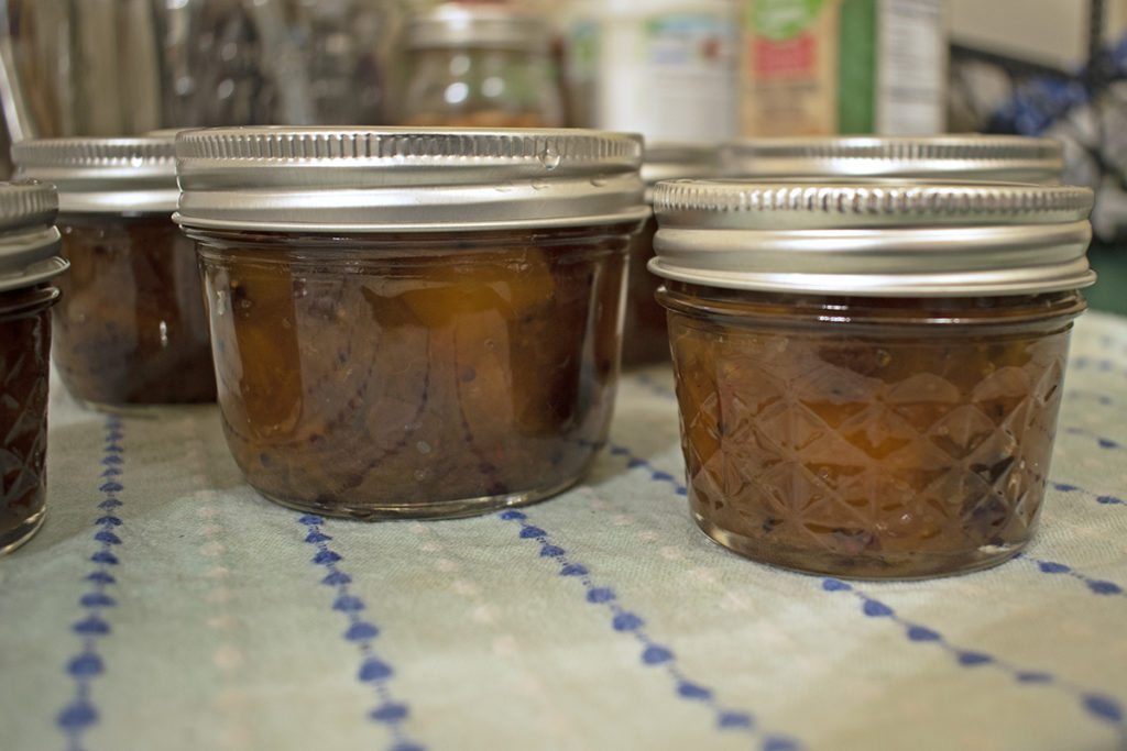 Several processed jars of chutney are resting on a doubled-up kitchen towel.