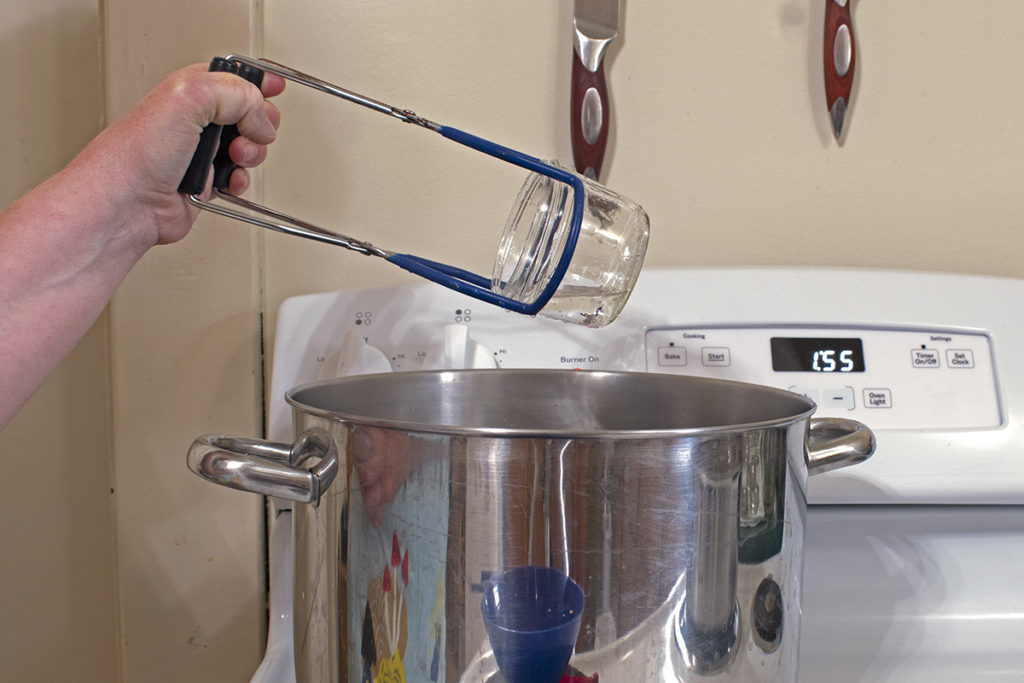 Hand lifting a jar from a water bath canner using a jar lifter.