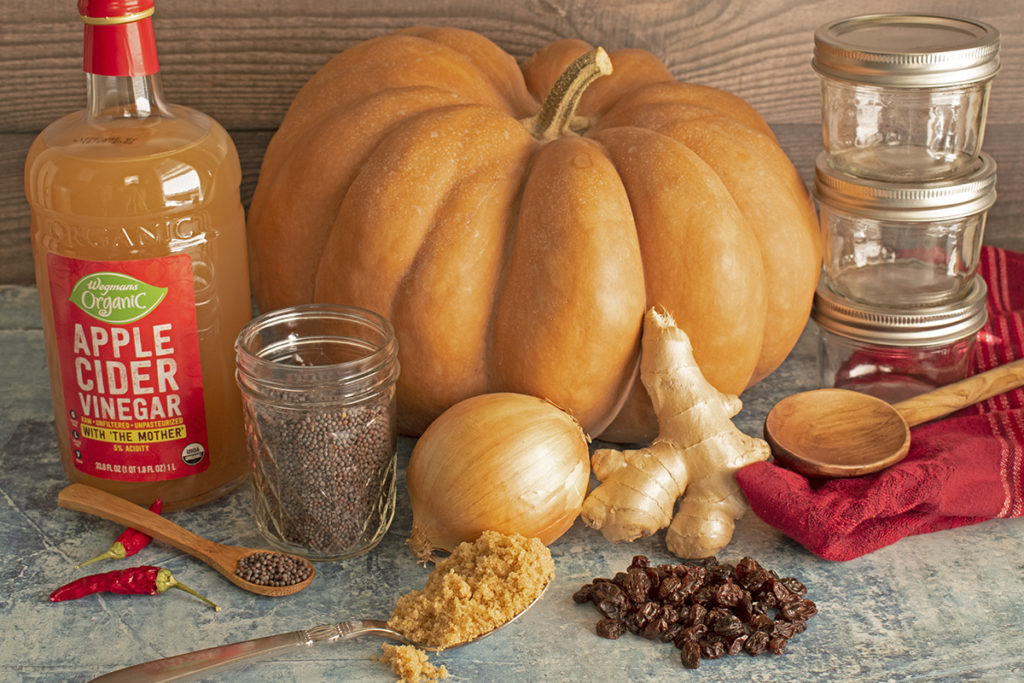 The ingredients for pumpkin chutney are laid out and ready to use: pumpkin, apple cider vinegar, mustard seeds, an onion, fresh ginger, raisins, and brown sugar.