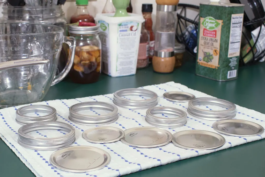 Canning jar lids and bands air dry on a doubled-up kitchen towel.