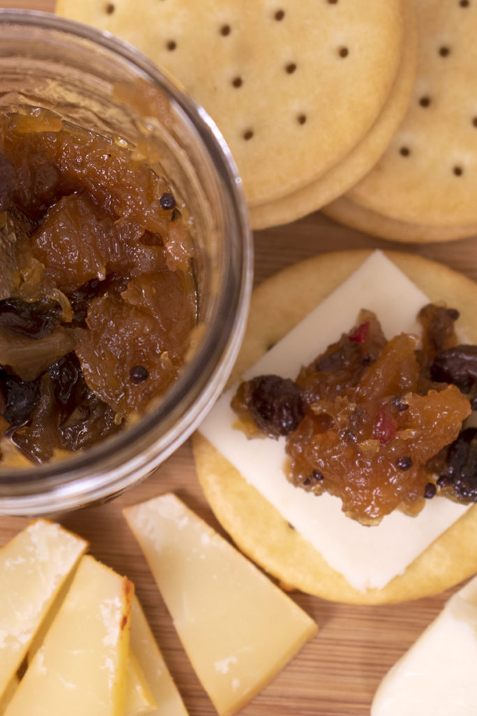 Close up of a jar of pumpkin chutney, chutney on top of cheese and crackers. 