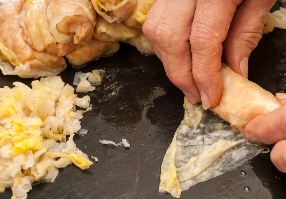 A hand is shown making sarmale with a pickled cabbage leaf.