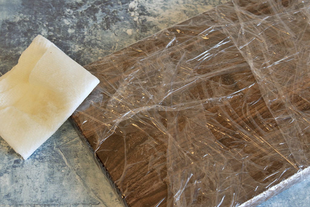 A wooden cutting board is wrapped in plastic wrap after having oil applied.